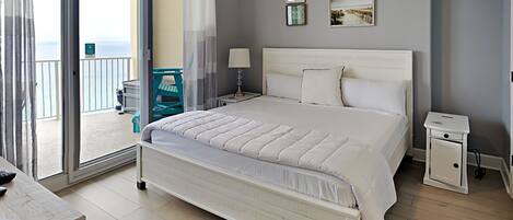 Quarto com cama grande, mesa de cabeceira e vista para a varanda.