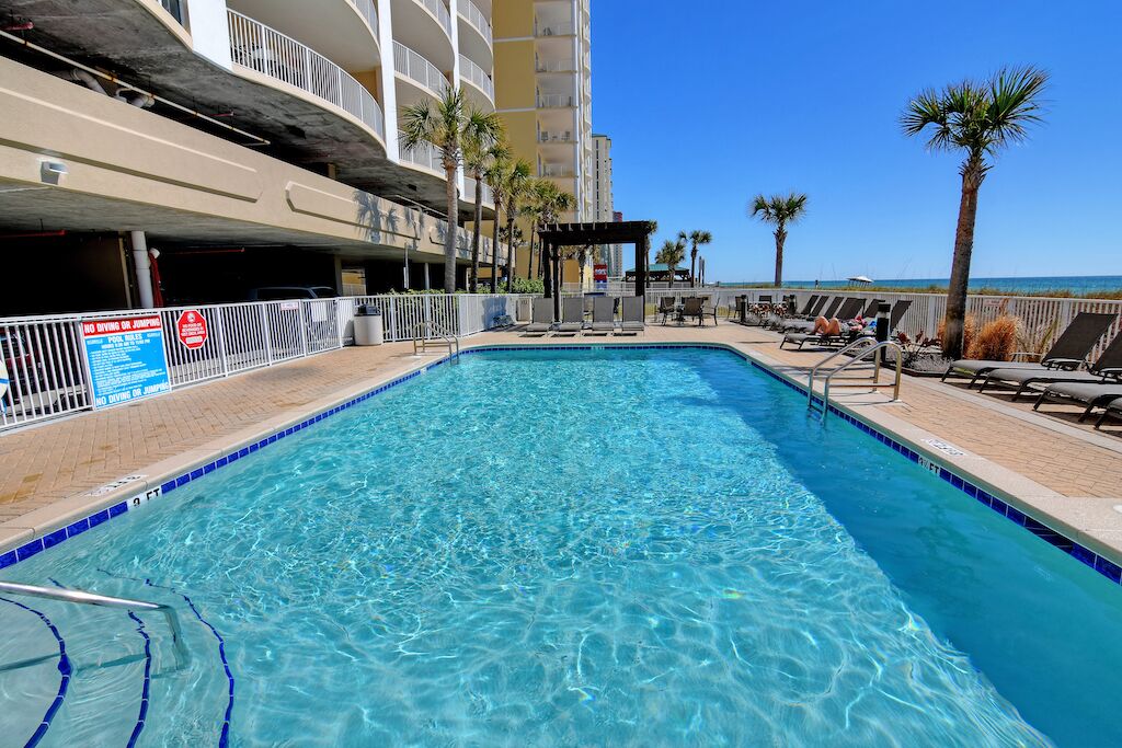 A swimming pool with lounge chairs and palm trees, surrounded by a building with balconies.