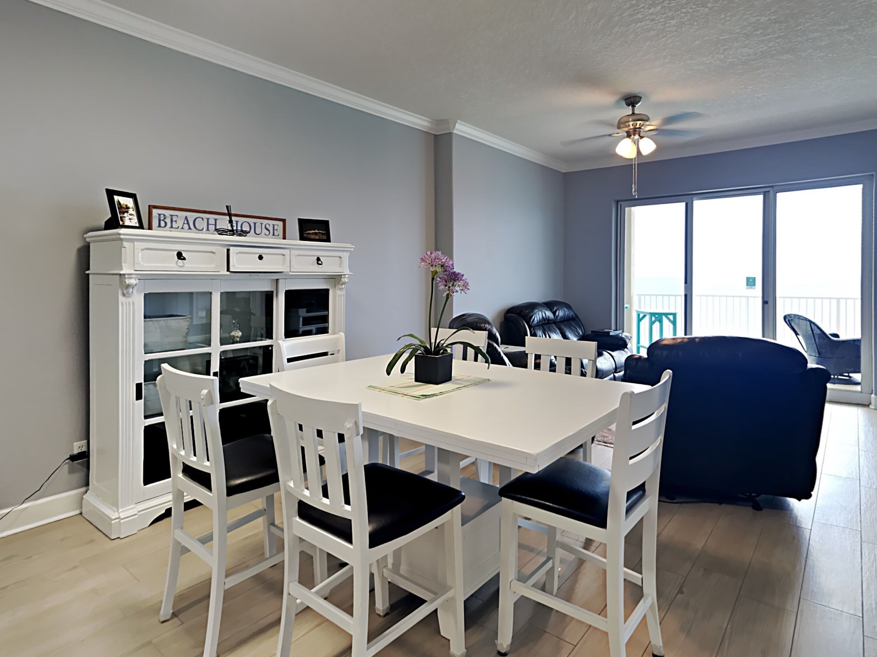 A dining area with a white table and chairs, a white cabinet with glass doors, and a ceiling fan.