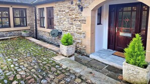 A stone building with a dark wooden door labeled "COLLETON," stone steps, and potted plants. - Colleton Cottage at Lovelady Shield (Alston)