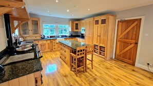 A spacious kitchen with wooden cabinets, a granite countertop, and a large island with bar stools. - Colleton Cottage at Lovelady Shield (Alston)