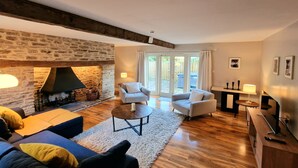 A cozy living room with a stone fireplace, wooden flooring, and a comfortable seating area with a sofa and armchairs. - Colleton Cottage at Lovelady Shield (Alston)