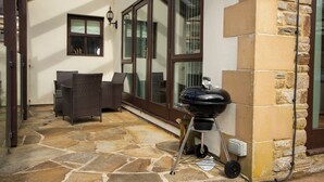 An outdoor patio with stone flooring, wicker furniture, a grill, and a glass door leading to a covered area. - Colleton Cottage at Lovelady Shield (Alston)
