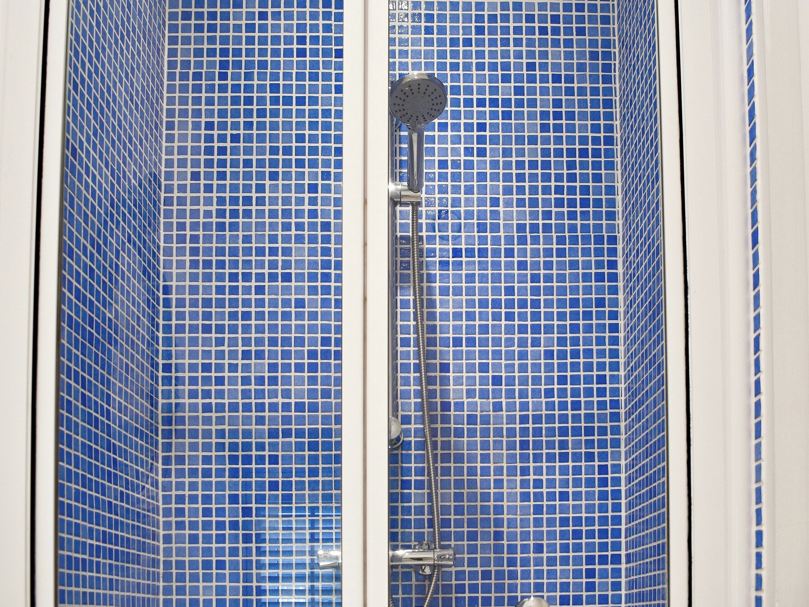 Une douche aux murs recouverts de mosaïques bleues et dotée d’un pommeau de douche amovible.