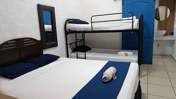 Une chambre avec un lit superposé, un lit simple, un miroir, un lavabo et une porte bleue.