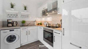 Een moderne keuken met witte kasten, een Bosch wasmachine, een inbouwoven en een magnetron.