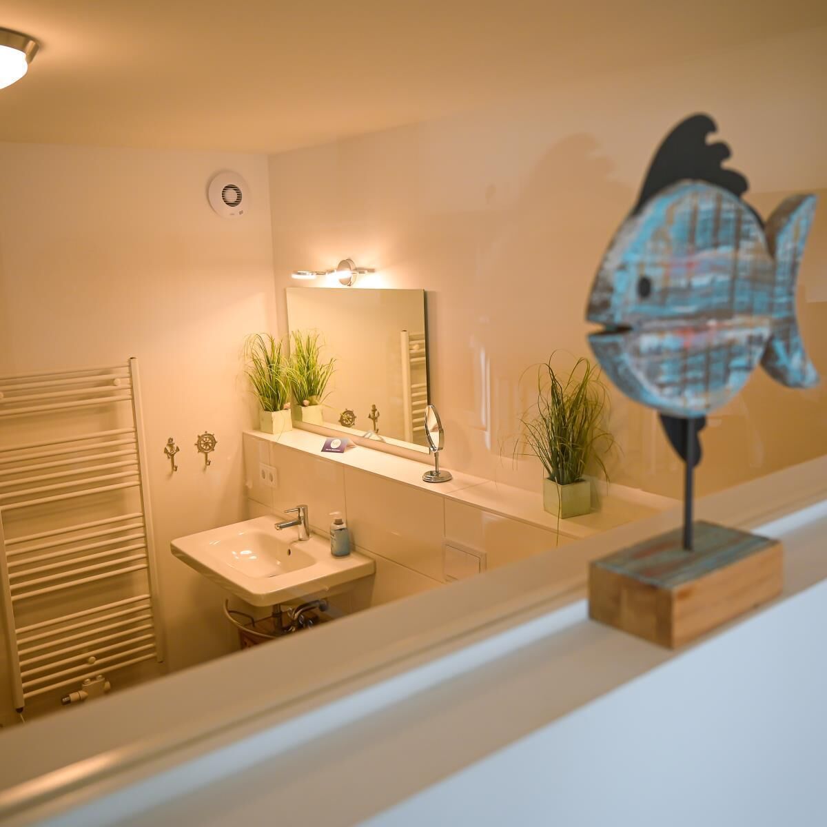 A bathroom with a sink, mirror, towel rack, and decorative fish sculpture.