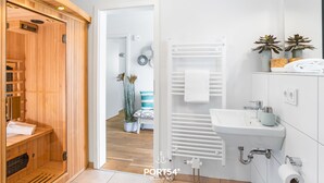 Een moderne badkamer met een houten sauna, een witte wastafel en een handdoekhouder.