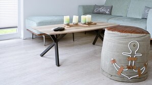 Een moderne woonkamer met een lichtkleurige bank, een houten salontafel met kaarsen, en een muur met decoraties op nautisch thema.