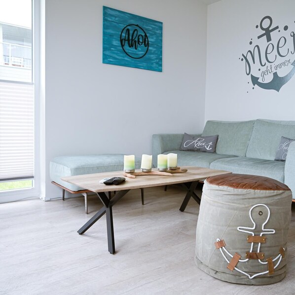 A modern living room with a light-colored sofa, a wooden coffee table with candles, and a wall with nautical-themed decorations.