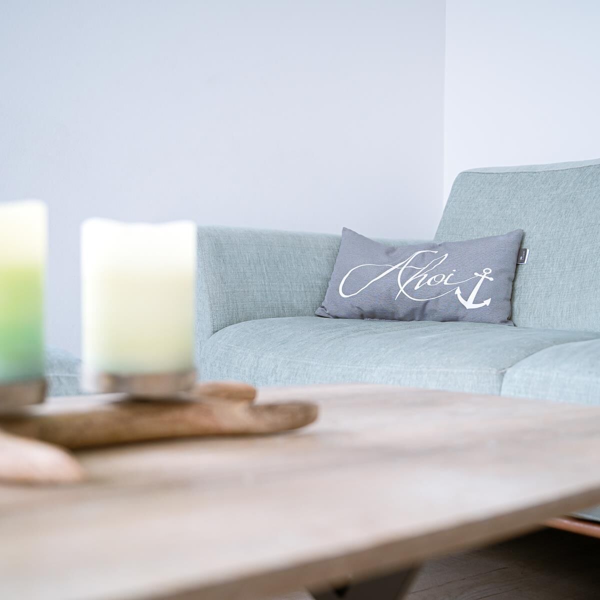 Un canapé gris clair avec un coussin orné d’un motif d’ancre blanche et du mot « Ahoi ».