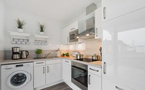 Una cocina moderna con armarios blancos, una lavadora Bosch, horno integrado y microondas.