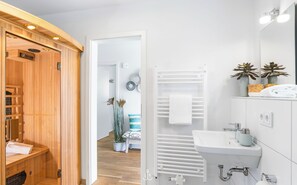 Un baño moderno con sauna de madera, un lavamanos blanco y un perchero para toallas.
