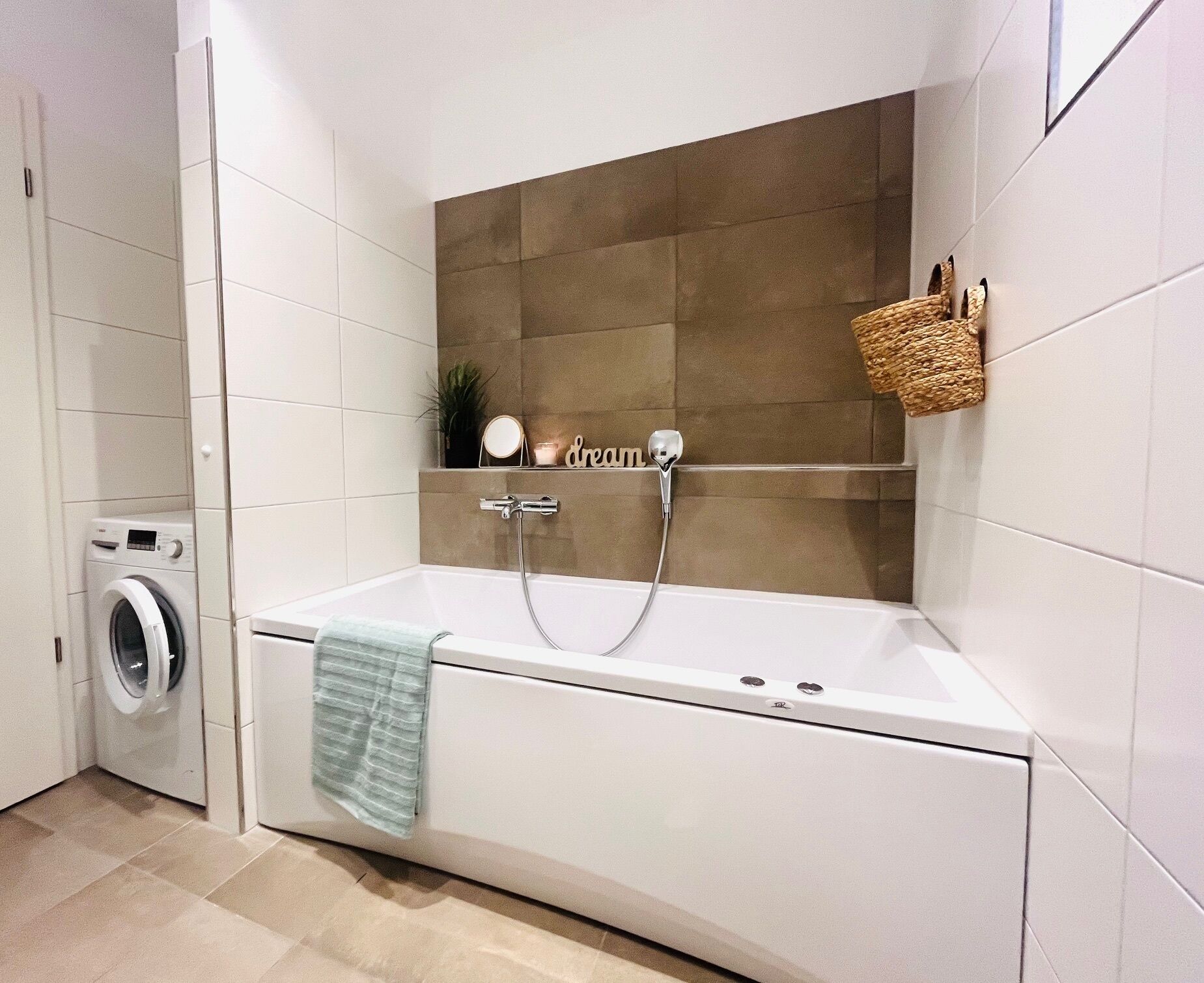 Een moderne badkamer met een badkuip, een wasmachine en een plank met decoratieve objecten.