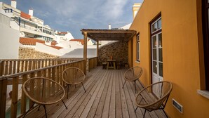 A wooden deck with wicker chairs, a stone wall, and a covered seating area. - Villa Galega (Torres Vedras)
