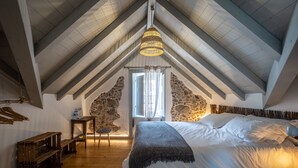 A bedroom with a sloped ceiling, a bed with white linens, a hanging light fixture, and stone walls. - Villa Galega (Torres Vedras)