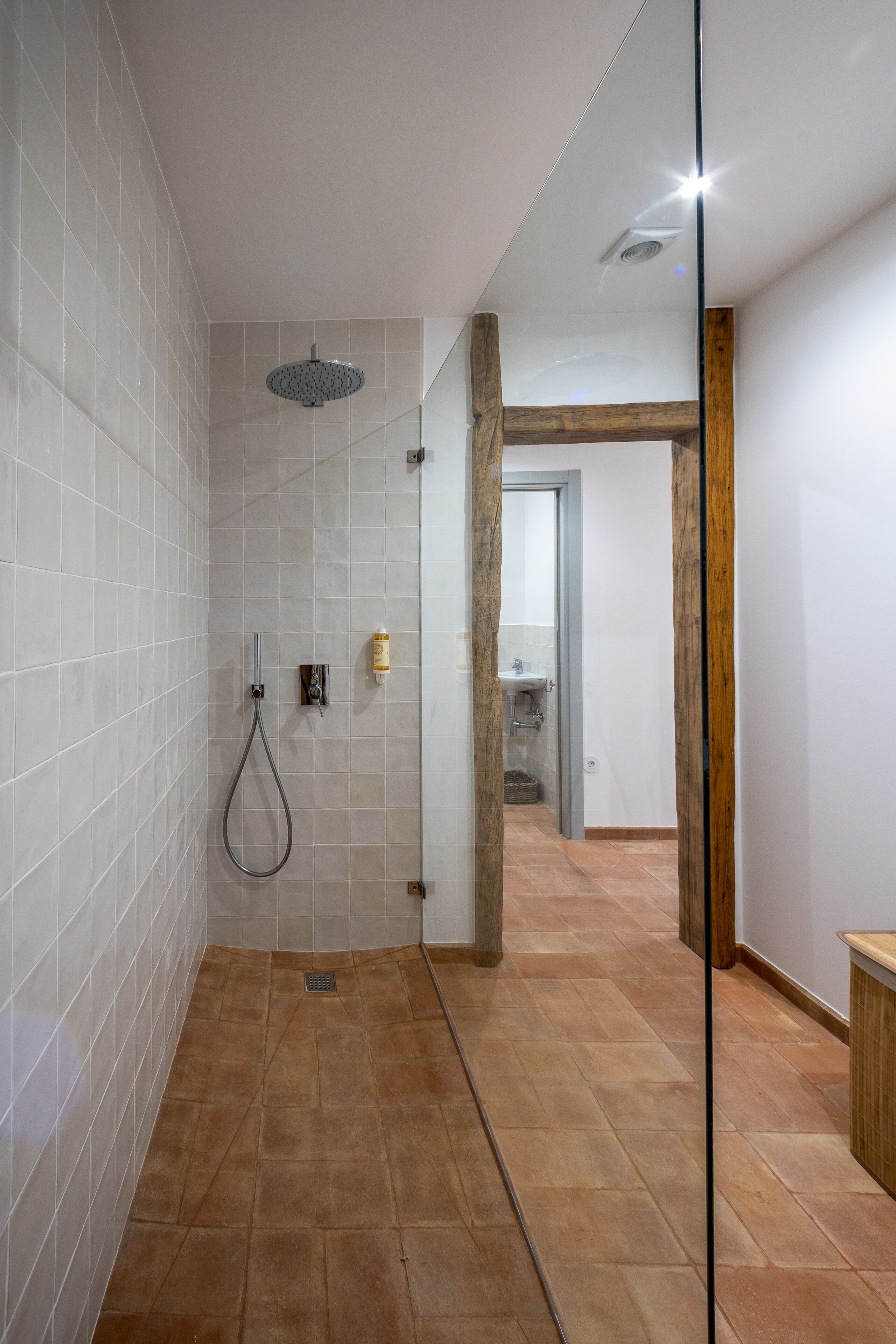 Un baño moderno con paredes de azulejos blancos, una zona de ducha y un marco de puerta de madera.