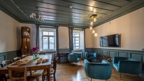 A dining area with a wooden table, chairs, a clock, and a TV mounted on the wall. - Villa Galega (Torres Vedras)