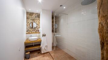 Een moderne badkamer met een accentmuur van steen, een houten wastafelmeubel, een ronde spiegel en een douche met een gebogen glazen deur.