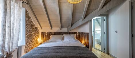 Un dormitorio con una cama grande, vigas de madera en el techo, una pared de piedra y una lámpara moderna.