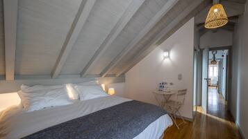 Un dormitorio con una cama grande, una mesita pequeña y una silla. El techo tiene vigas de madera y una lámpara colgante.