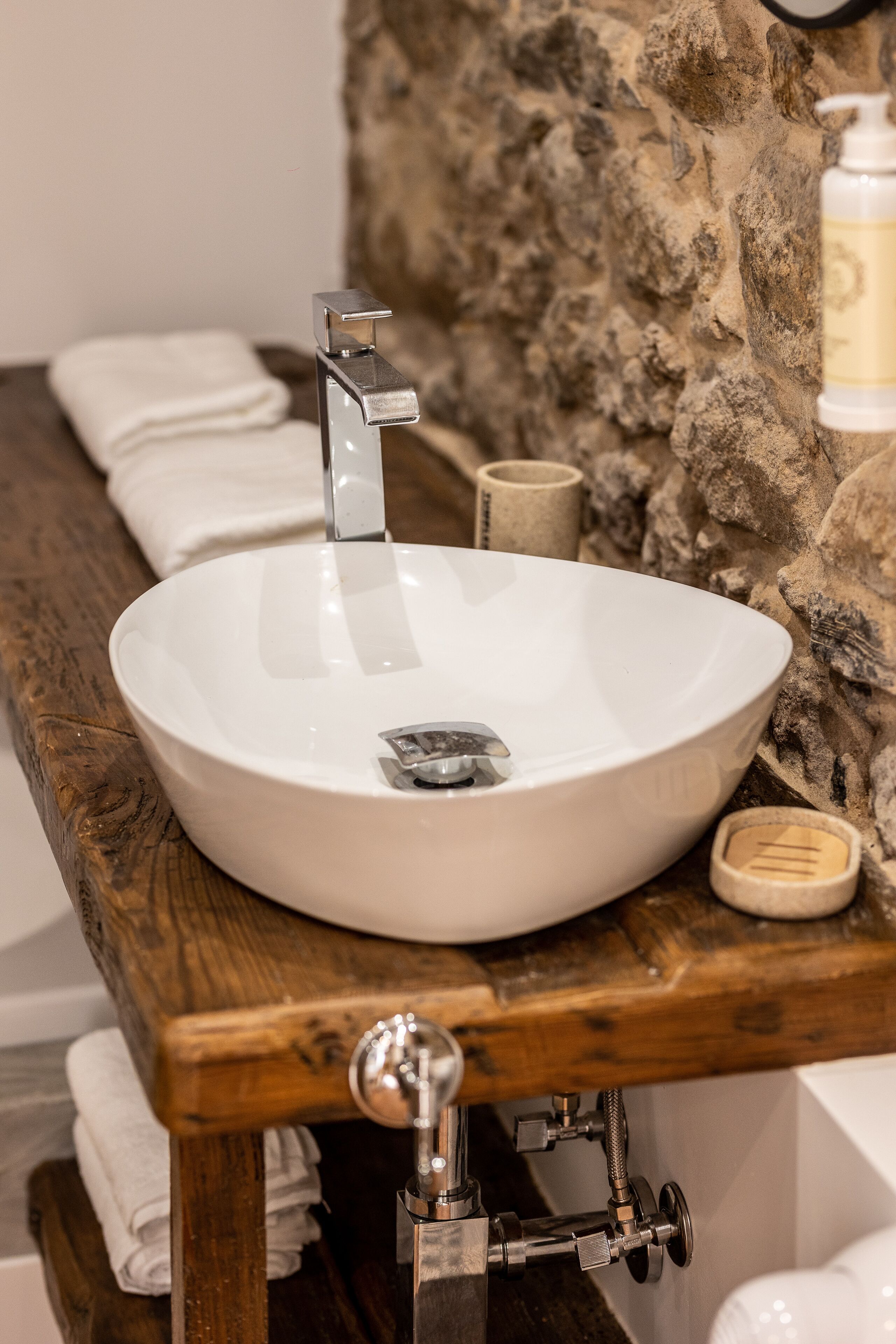 A white ceramic sink with a modern faucet, mounted on a wooden countertop with a stone wall backdrop.