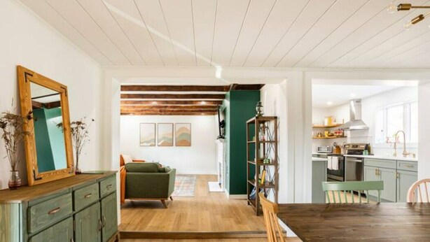 A spacious living room with a wooden floor, a green sofa, and a dining area with a wooden table and chairs. - Kin Cottage Accord (Accord)