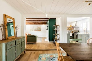 A spacious living room with a wooden floor, a green sofa, and a dining area with a wooden table and chairs.