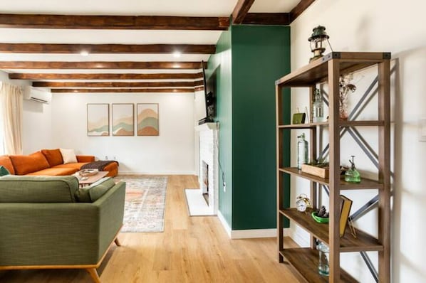 A cozy living room with a green sofa, wooden beams on the ceiling, and a green accent wall.