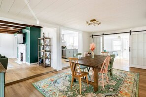 A spacious dining area with a wooden table and chairs, a decorative rug, and a modern chandelier.
