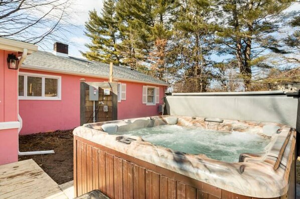 Ein Whirlpool in einem Garten mit einem rosa Haus und Bäumen im Hintergrund.
