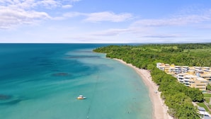 Un complejo turístico costero con playa, aguas turquesas cristalinas y exuberante vegetación.