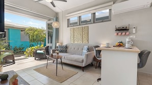 Un espacio habitable moderno con sofá, mesa de centro y comedor. Cuenta con un balcón con plantas y vistas al exterior.