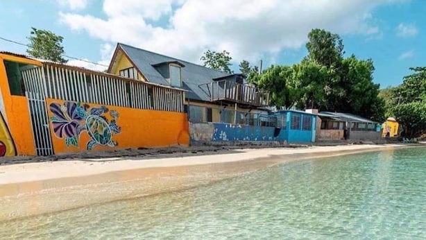 Una playa con aguas poco profundas y transparentes, edificios coloridos y un mural en una de las edificaciones.