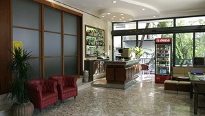 A lobby with red leather chairs, a bar area, a Coca-Cola refrigerator, and a large window with a view of trees. - Hotel Baltic (Rimini)