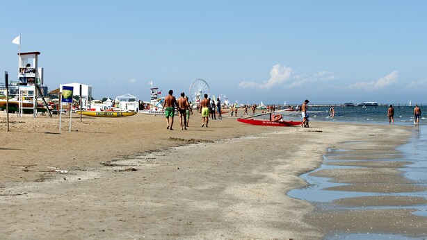 A beach with a lifeguard tower, boats, and people enjoying the shore. - Hotel Baltic (Rimini)