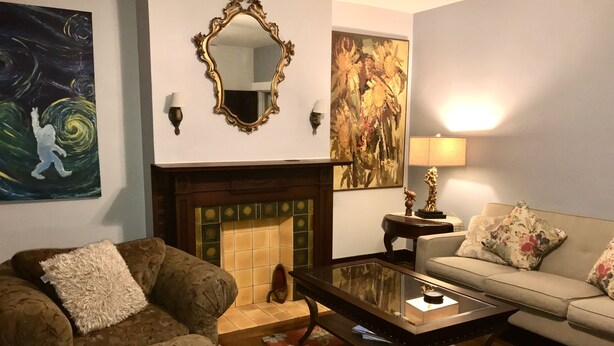 A living room with a fireplace, a sofa, a coffee table, and two paintings on the wall. - Eclectic Historic Sunny Vista Home with City Views, Northshore (Pittsburgh)