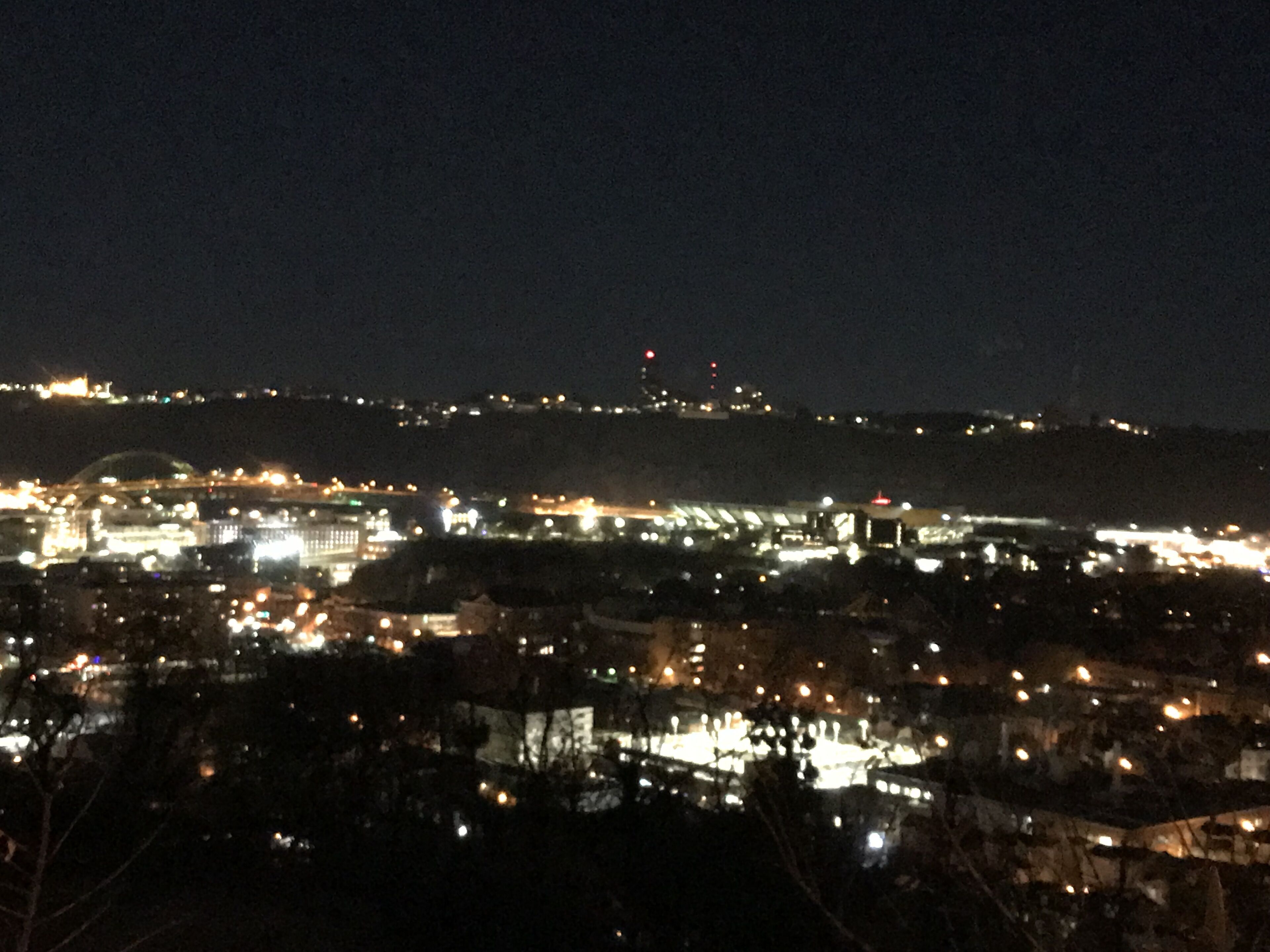 A nighttime cityscape with illuminated buildings and a hill in the background.