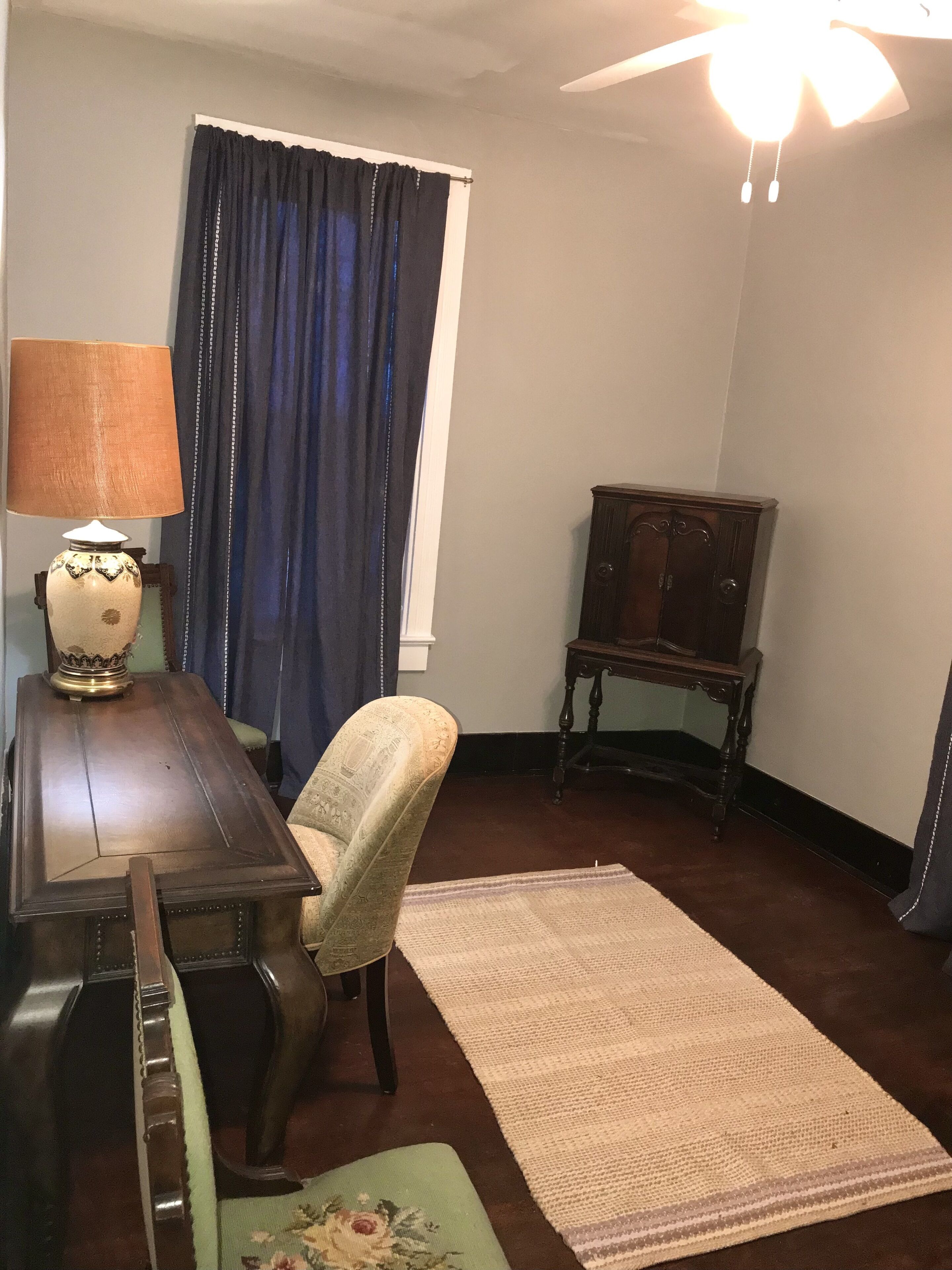 Una habitación con escritorio de madera, una silla, lámpara, armario, alfombra y ventilador de techo.