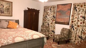 A bedroom with a bed, two chairs, a wooden wardrobe, floral curtains, and a painting on the wall. - Eclectic Historic Sunny Vista Home with City Views, Northshore (Pittsburgh)