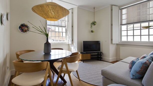 A modern living room with a glass-top dining table, wooden chairs, a sofa, a TV, and a large window with natural light. - Boutique Rentals- D*OURO Ribeira w/parking (Porto)