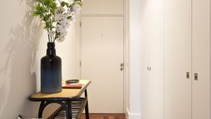 A hallway with a radiator, a table with a vase of flowers, a bench, and white wardrobes. - Boutique Rentals- D*OURO Ribeira w/parking (Porto)