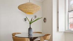 A dining area with a round table, wooden chairs, a woven pendant light, and a vase with green plants. - Boutique Rentals- D*OURO Ribeira w/parking (Porto)