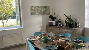 Un coin repas avec une table en bois, des chaises de couleur turquoise et une vue sur la verdure environnante.