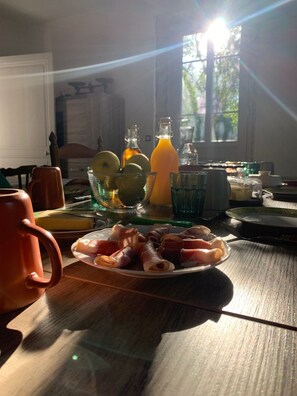 A breakfast table with a plate of ham, a bowl of fruit, and a glass of orange juice.