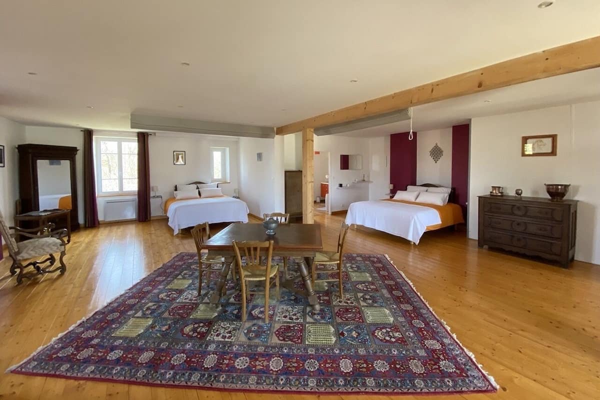 Una habitación amplia con dos camas, una mesa de comedor con sillas y un tapete grande con estampado.