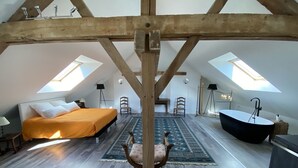 Une chambre aménagée dans un espace ouvert, avec un lit, une chaise, une baignoire et des fenêtres de toit.
