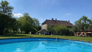 Une piscine dont le bord est recouvert de carrelage, entourée d’une pelouse et d’arbres.