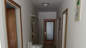 Ein Flur mit einem Badezimmer, das ein Waschbecken, Toilettenpapier und einen Spiegel zeigt.