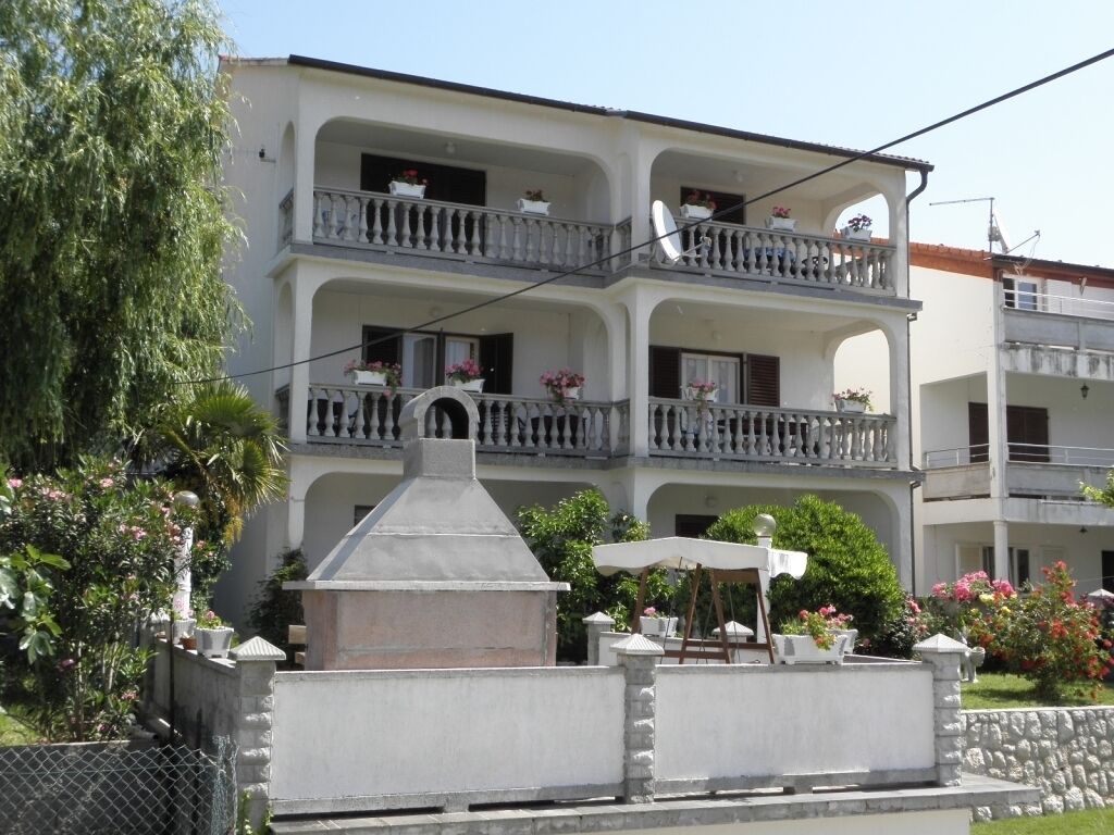 Un edificio de varios pisos con balcones, zona de barbacoa y mobiliario exterior.